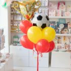 Ramos de globo fútbol España con Helio en rojo y amarillo con balón, copa y base decorativa.