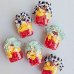 Tarritos de chuches España decorados con tela vichy y rellenos de gominolas rojas y amarillas.