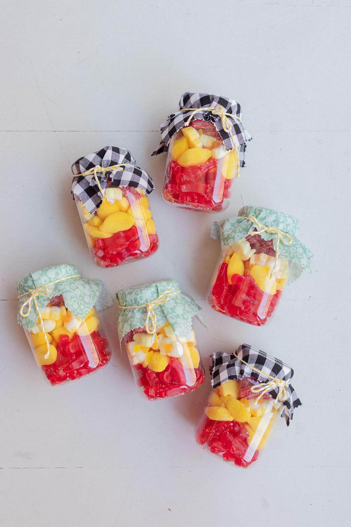 Tarritos chuches España Tarritos de chuches España decorados con tela vichy y rellenos de gominolas rojas y amarillas.